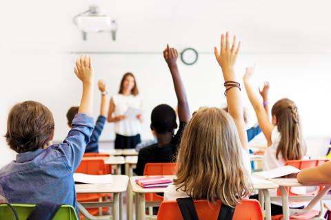Kinderen zitten in de klas en steken hun hand op