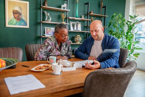 Man en vrouw zitten aan tafel in de woonkamer. Het is een kleurrijke ruimte met een groene muur