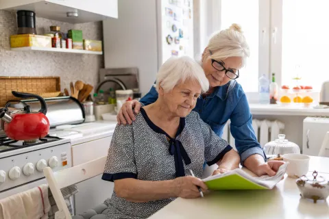 Een jongere vrouw helpt een oudere vrouw met een formulier
