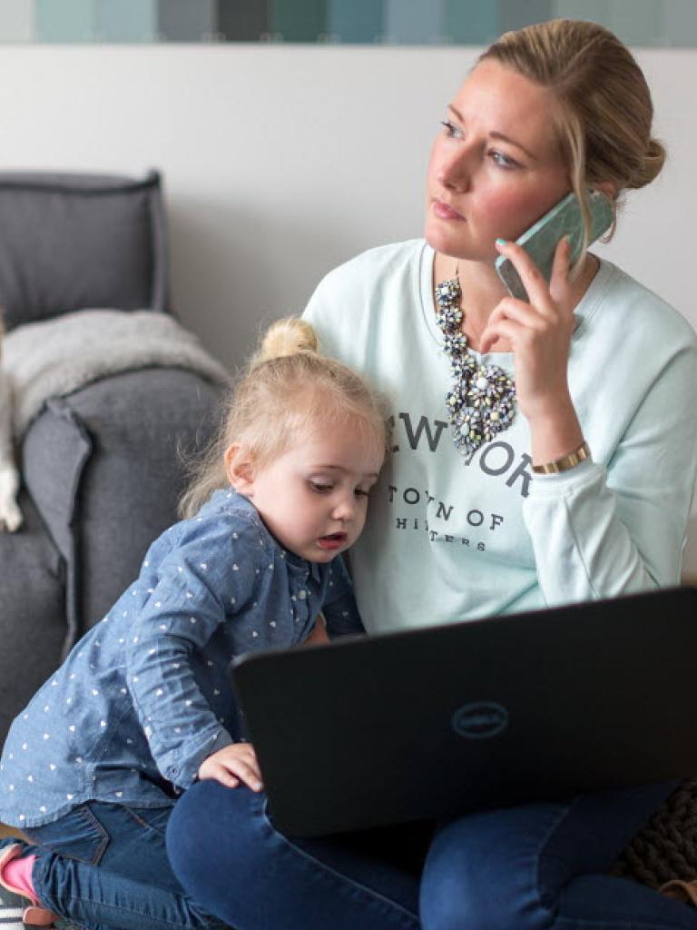 Een vrouw aan de telefoon met een laptop en een kind op schoot