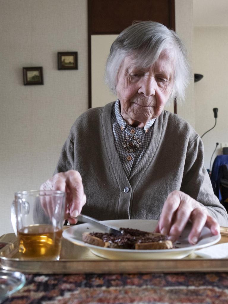 Oudere vrouw smeert een boterham thuis aan tafel