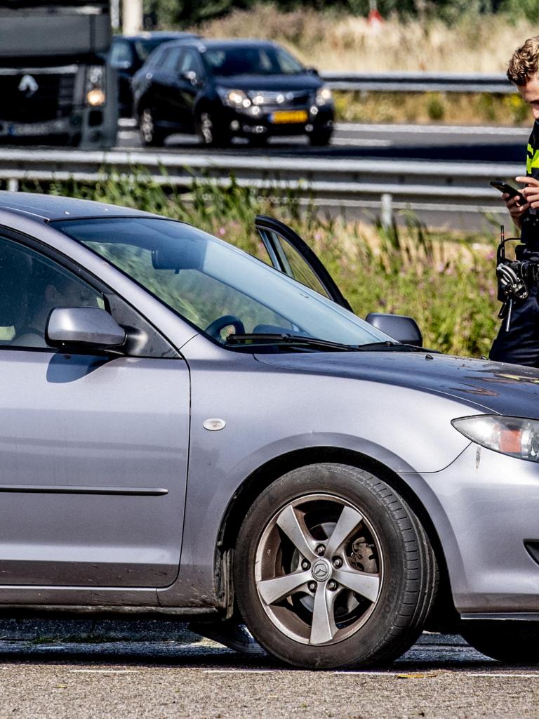 Een agent staat naast een auto bij een drukke weg en schrijft een boete uit. 