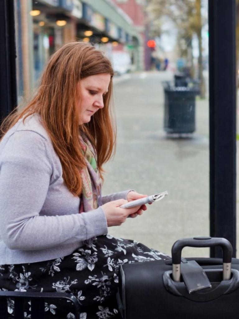 Vrouw zit met koffer bij bushalte