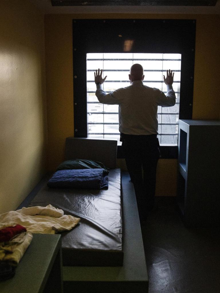 Kale man houdt zijn handen tegen de tralies van zijn gevangeniscel en kijkt naar buiten