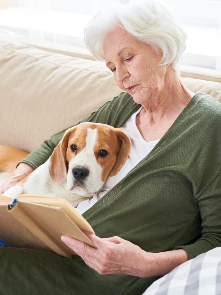 Vrouw zit met hond op de bank een boek te lezen