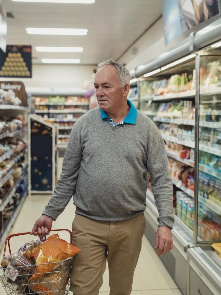 Senior man loopt met gevuld winkelmandje in supermarkt