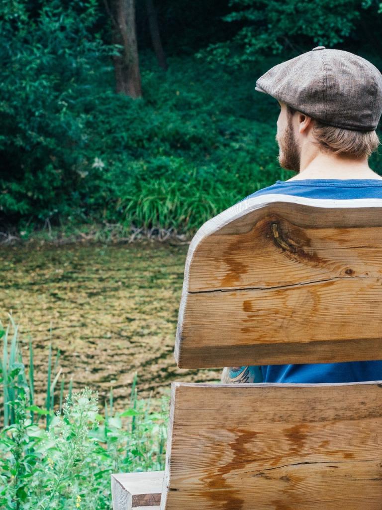 Man zit in de natuur op een bank. Hij is van achter gefotografeerd.