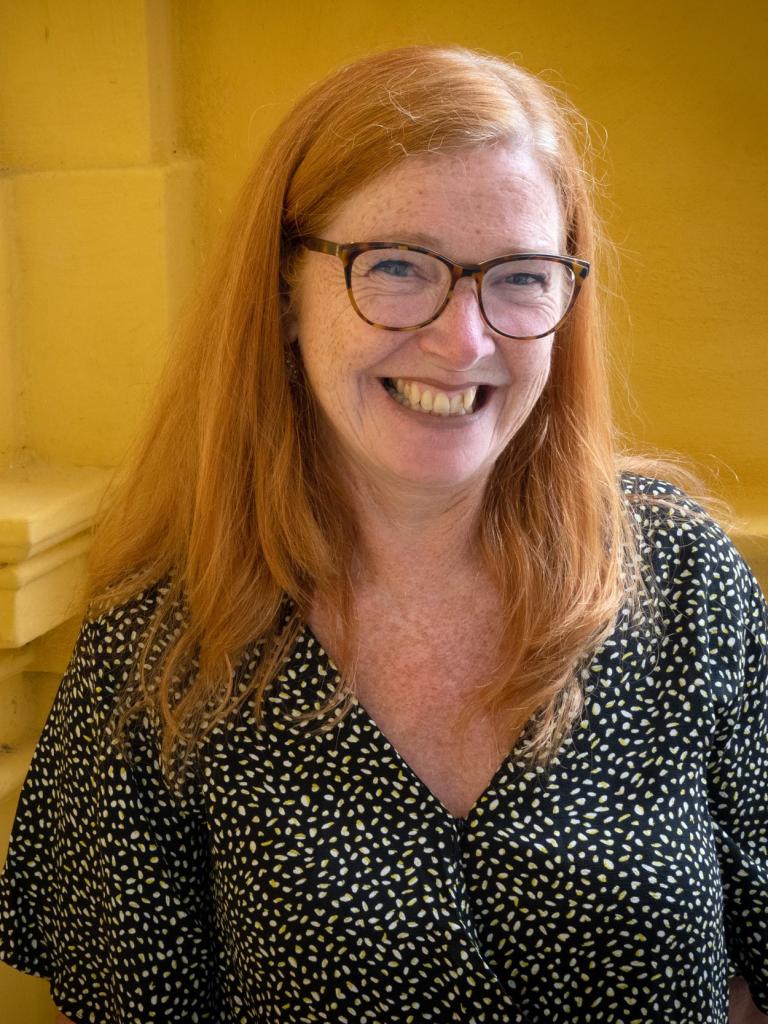 Lachende vrouw (mantelzorger Ingrid Keestra) met lang rood haar, een bril en draagt een zwart shirt