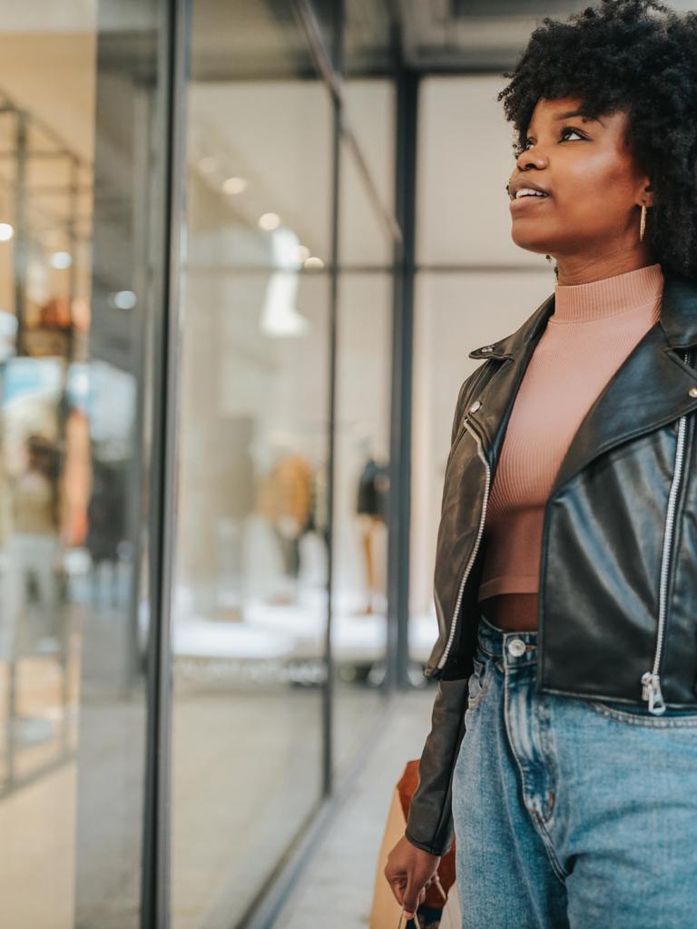 Zwarte jonge vrouw staat buiten voor de etalage van een kledingwinkel