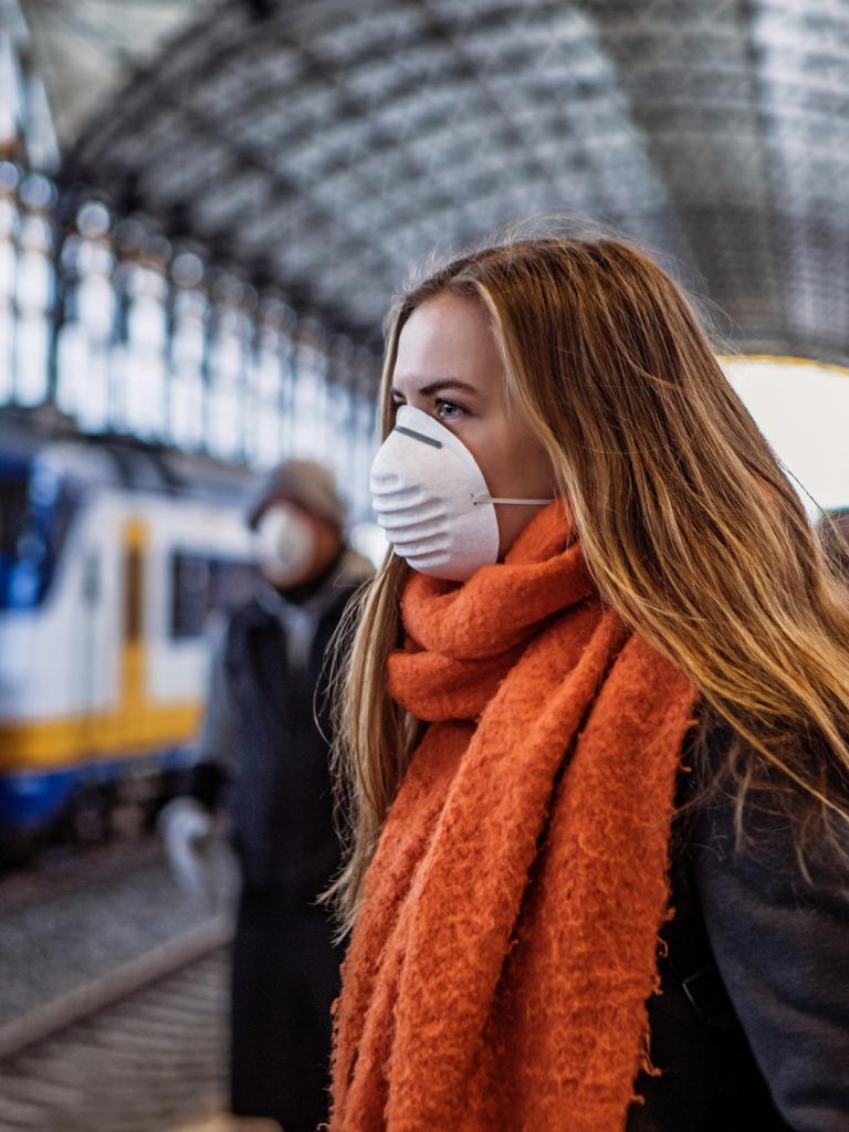 Jonge vrouw met een mondkapje wacht op een trein