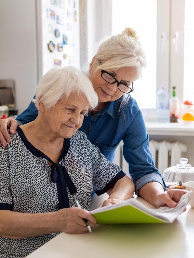 Een jongere vrouw helpt een oudere vrouw met een formulier
