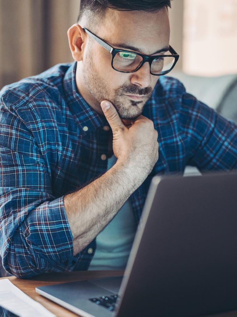 Man van middelbare leeftijd met bril en geruite blouse kijkt zorgelijk naar zijn laptop.