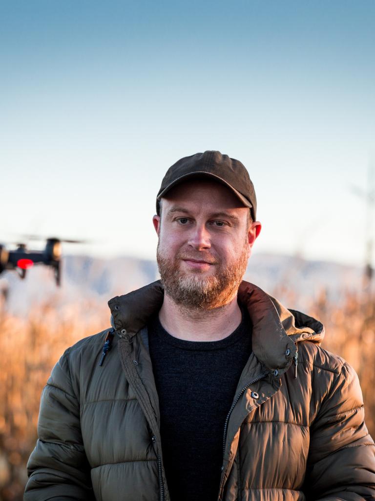 Man met petje op en rode baard staat buiten en vliegt met een drone