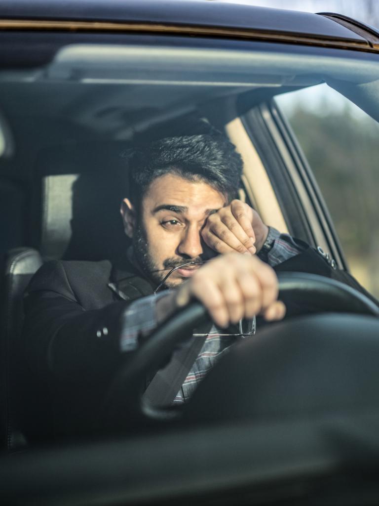 Een jonge man zit in een auto en wrijft uit moeheid in zijn ogen