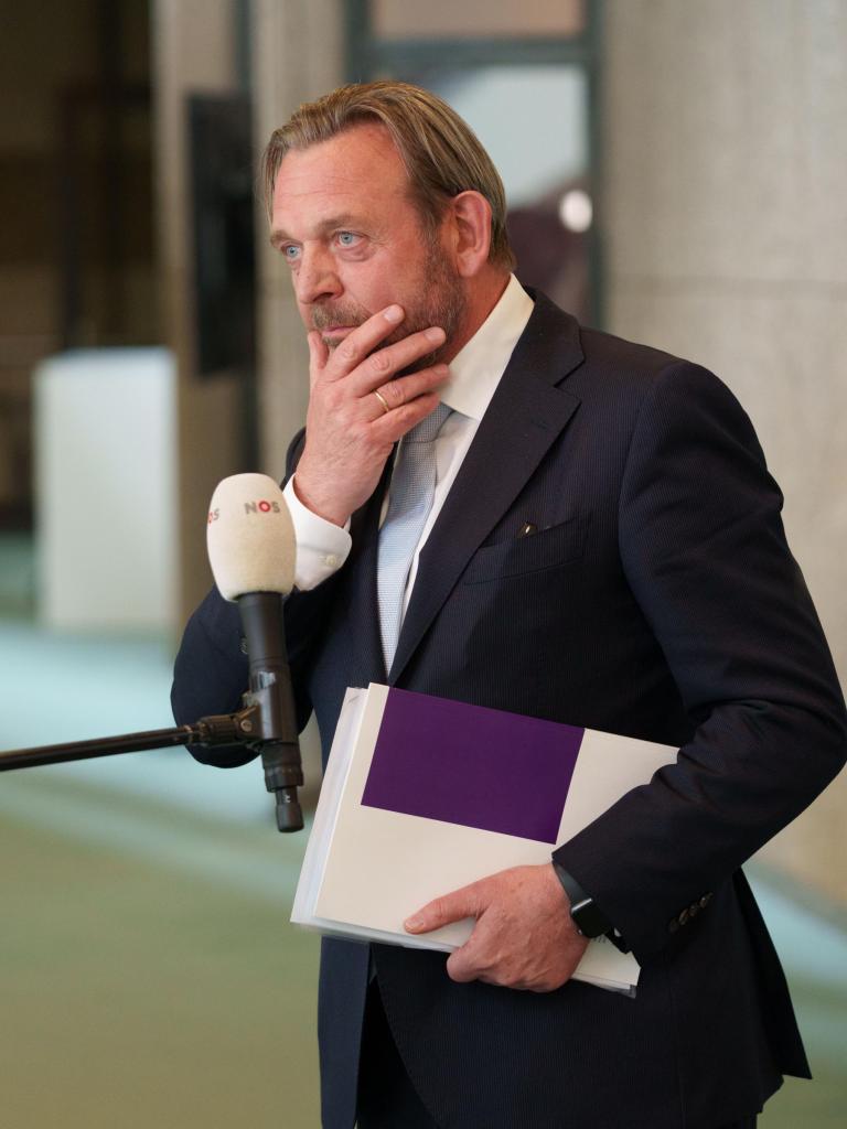 Man met baard (Reinier van Zutphen, Nationale ombudsman). Hij draagt een zwart pak, heeft zijn hand op de kin en houdt in de andere hand documenten