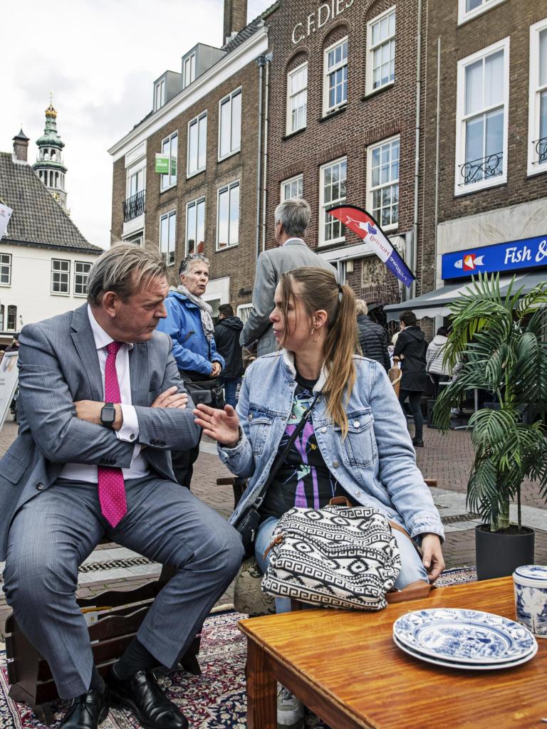 De Nationale ombudsman op bezoek in Zeeland. Hij is in gesprek met een vrouw met donkerbruin lang haar. Ze bevinden zich op een plein.