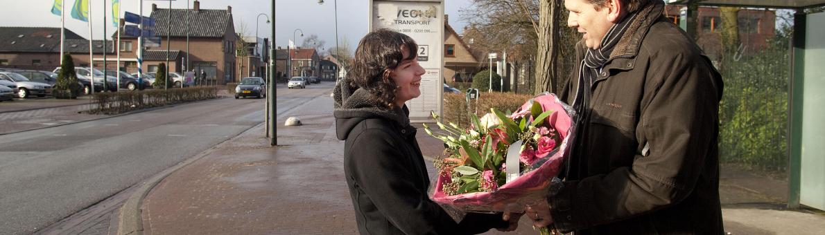 Foto van een man die op straat een bos bloemen geeft aan een vrouw