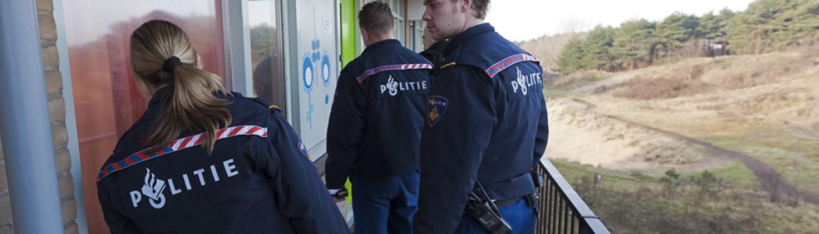 Drie politieagenten bij een woning, natuur op de achtergrond