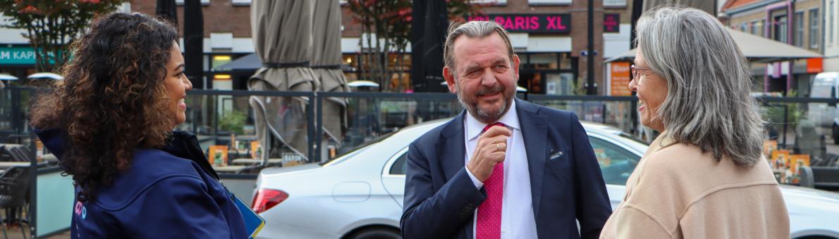 Nationale ombudsman Reinier van Zutphen in gesprek met collega Mira (jonge vrouw met bruin krullend haar) en een vrouw op straat (middelbare leeftijd, grijs haar)