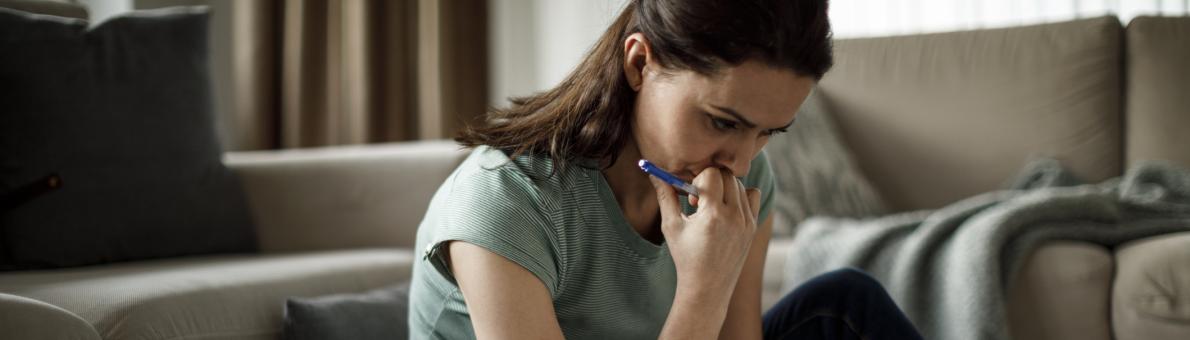 Vrouw zit op de grond en heeft papieren in haar hand. Voor haar staat ook een laptop.