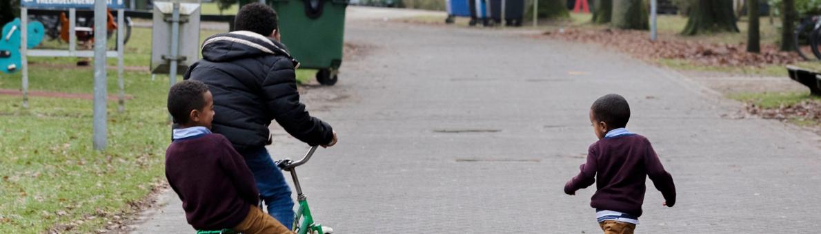 Drie spelende kinderen in het AZC, rennend en op de fiets