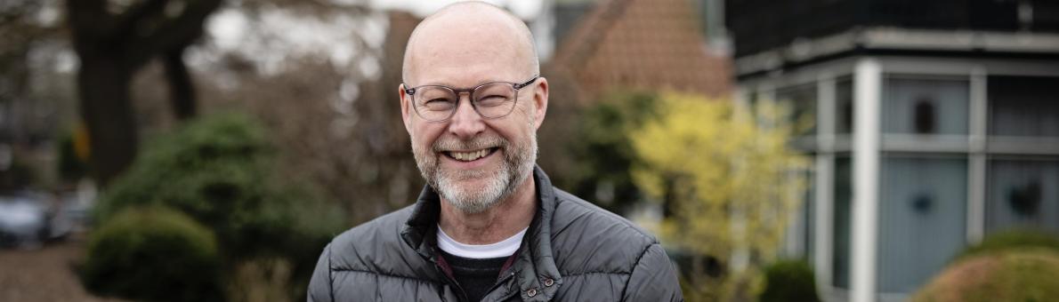 Een man staat lachend voor een tuin en poseert voor de foto Een man staat lachend voor een tuin en poseert voor de foto