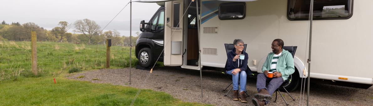 Een ouder echtpaar zit voor een camper