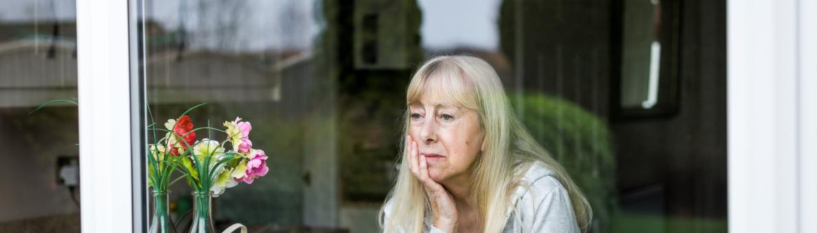 Senior vrouw kijkt zorgelijk uit het raam Senior vrouw kijkt zorgelijk uit het raam