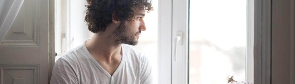 Man met koffie in hand kijkt uit zijn raam