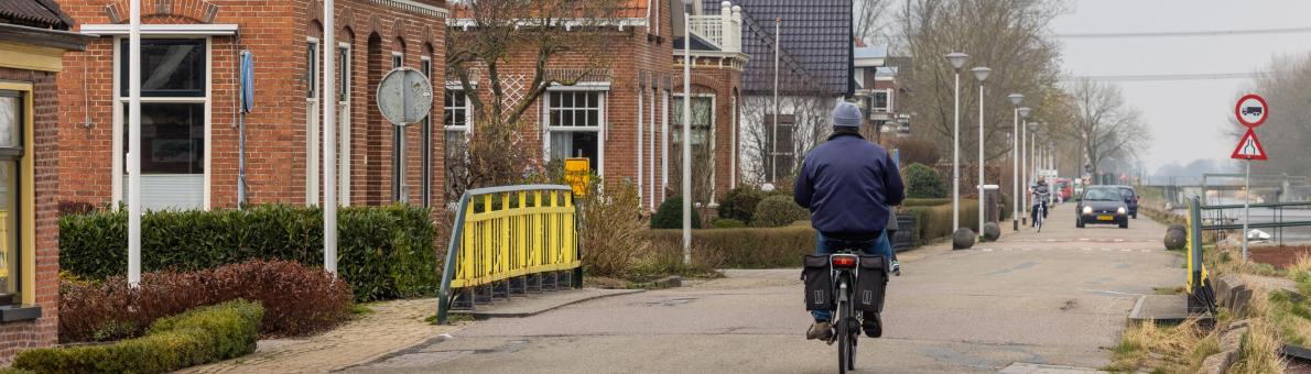 Een man op een gemotoriseerde fiets rijdt langs een aantal huizen in de provincie Groningen