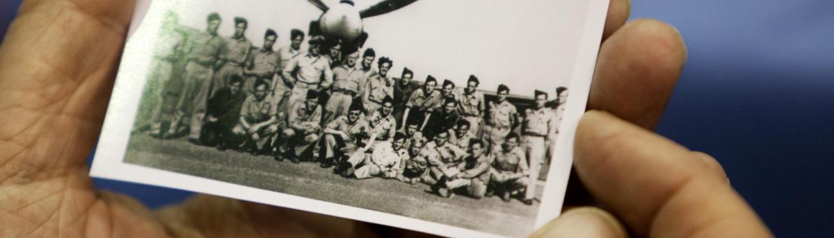 persoon houdt oude foto vast met militairen voor een vliegtuig