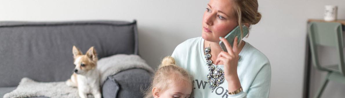 Een vrouw aan de telefoon met een laptop en een kind op schoot