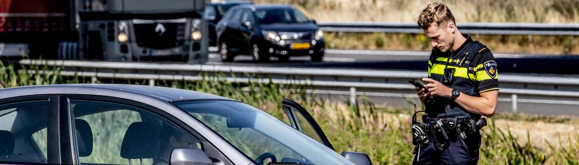 Een agent staat naast een auto bij een drukke weg en schrijft een boete uit. 