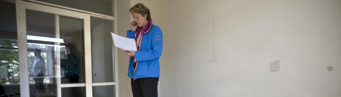 Vrouw met blauwe jas staat in lege kamer met matras op de grond