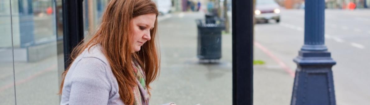 Vrouw zit met koffer bij bushalte