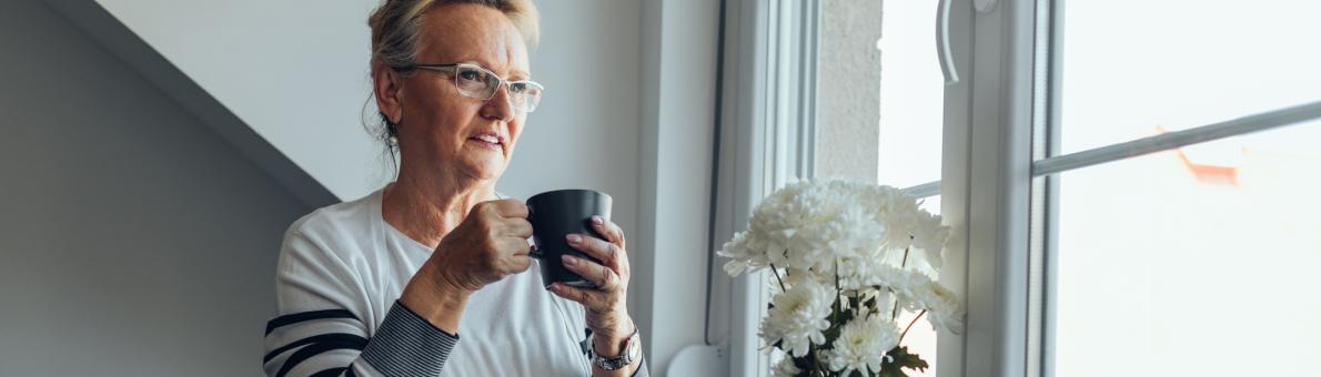 Vrouw zit bij het raam met een kop koffie