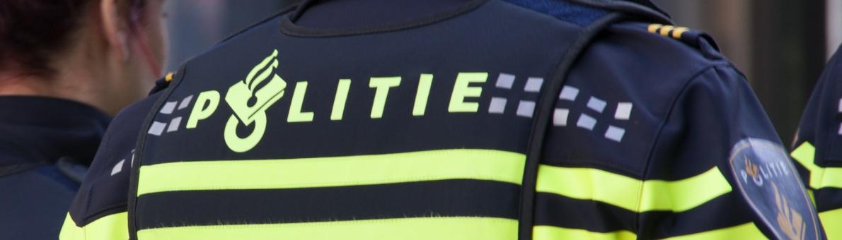 Een politie agent van de achterkant gefotografeerd. We zien zijn rug en politiekleding.