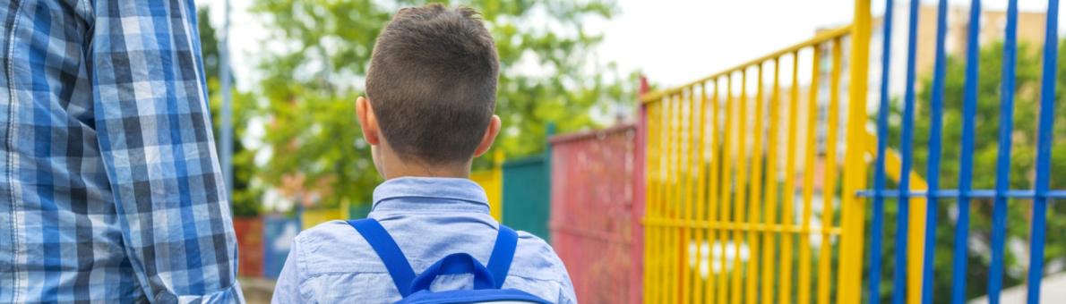 Jongetje met blauw shirt en rugzak loopt bij z'n vader aan de hand