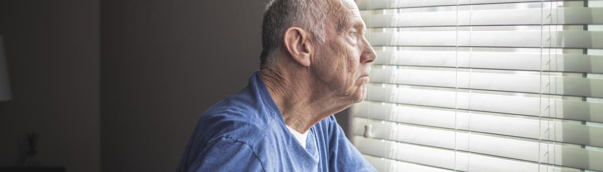 Een oudere man leunt op zijn rollator en kijkt uit het raam