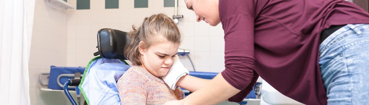 Verzorgster helpt meisje in rolstoel met wassen van het gezicht
