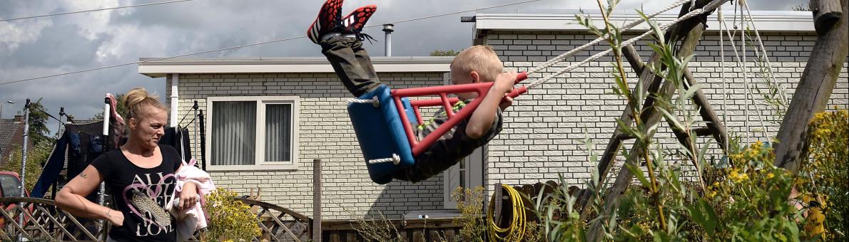 vrouw kijkt naar schommelend kind in tuin