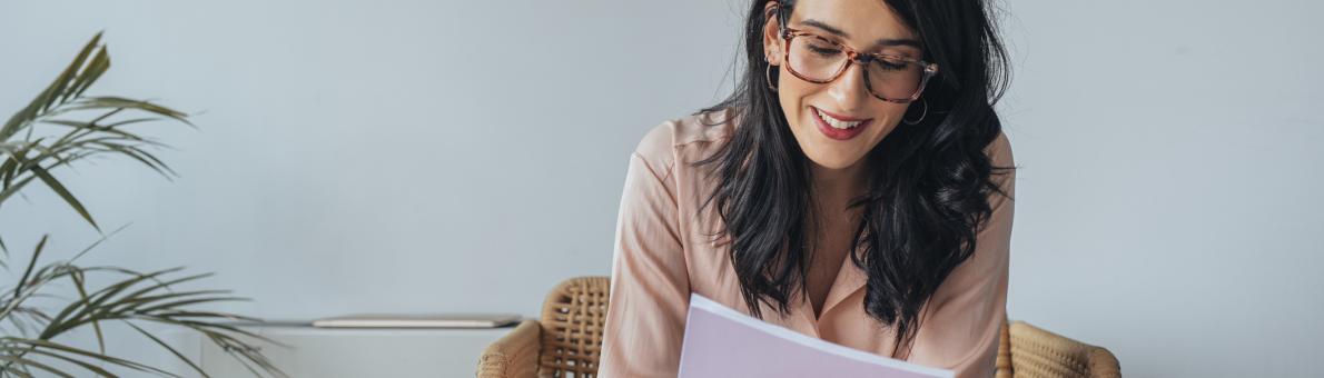 Vrouw met lang donker haar, donkere bril en roze blouse leest folders