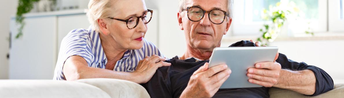 Ouder stel zit op de bank met iPad in de hand