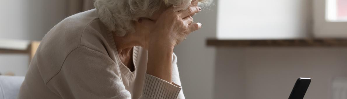 Een oudere vrouw met haar met smartphone in haar hand. Ze leunt met haar hoofd op haar andere hand.