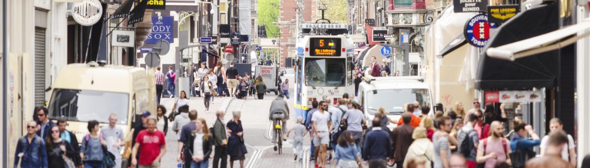 Winkelstraat in Amsterdam. Mensen lopen op straat, een tram rijdt in de verte