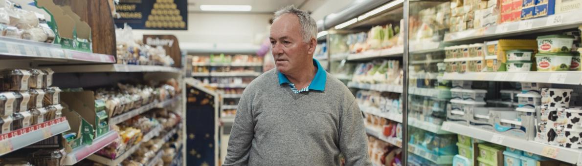 Senior man loopt met gevuld winkelmandje in supermarkt