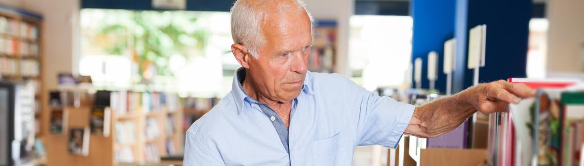 Senior man met boek in zijn hand in een boekenwinkel