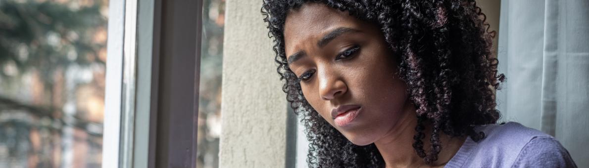 Vrouw kijkt zorgelijk op haar mobiel en staat bij het raam