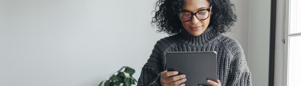 Vrouw met donkere krullen en grijze trui leest magazine online op tablet