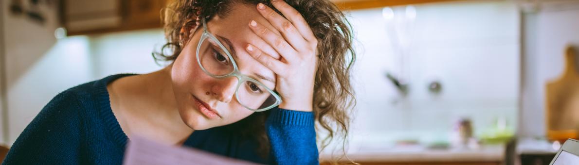 Vrouw zit achter de laptop en kijkt bezorgd naar een brief in haar handen